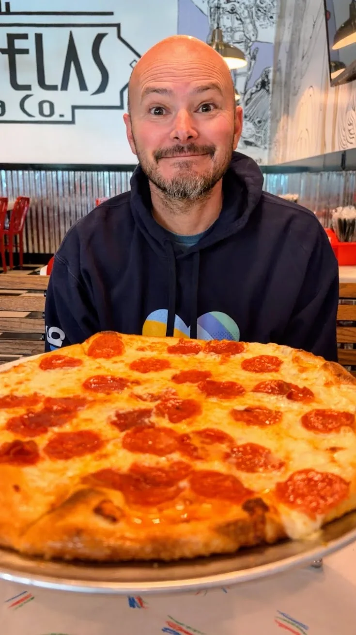 Mike Stevens sitting behind a large pepperoni pizza