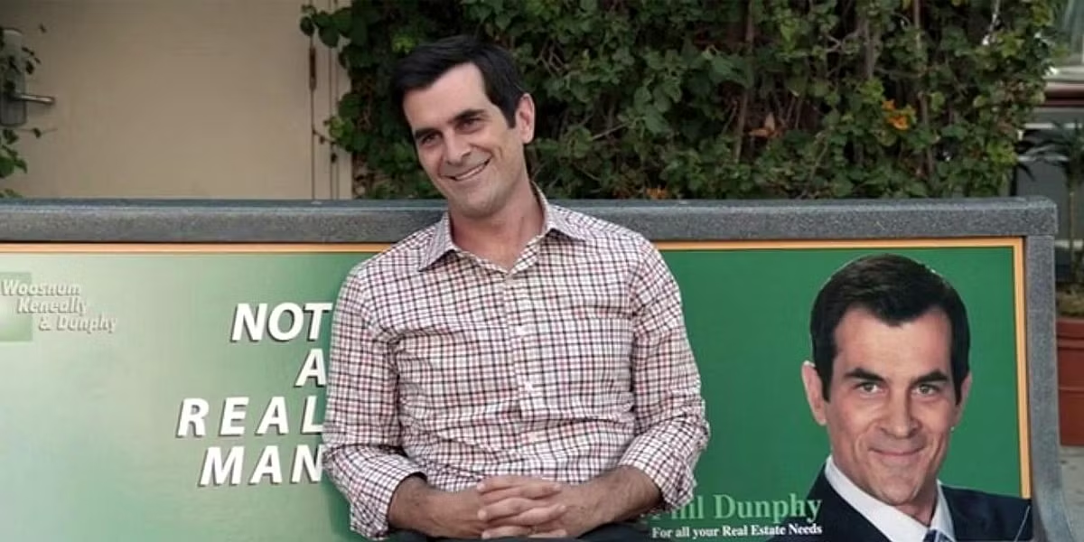 Phil Dunphy standing beside a real-estate advertisement featuring his own portrait in Modern Family